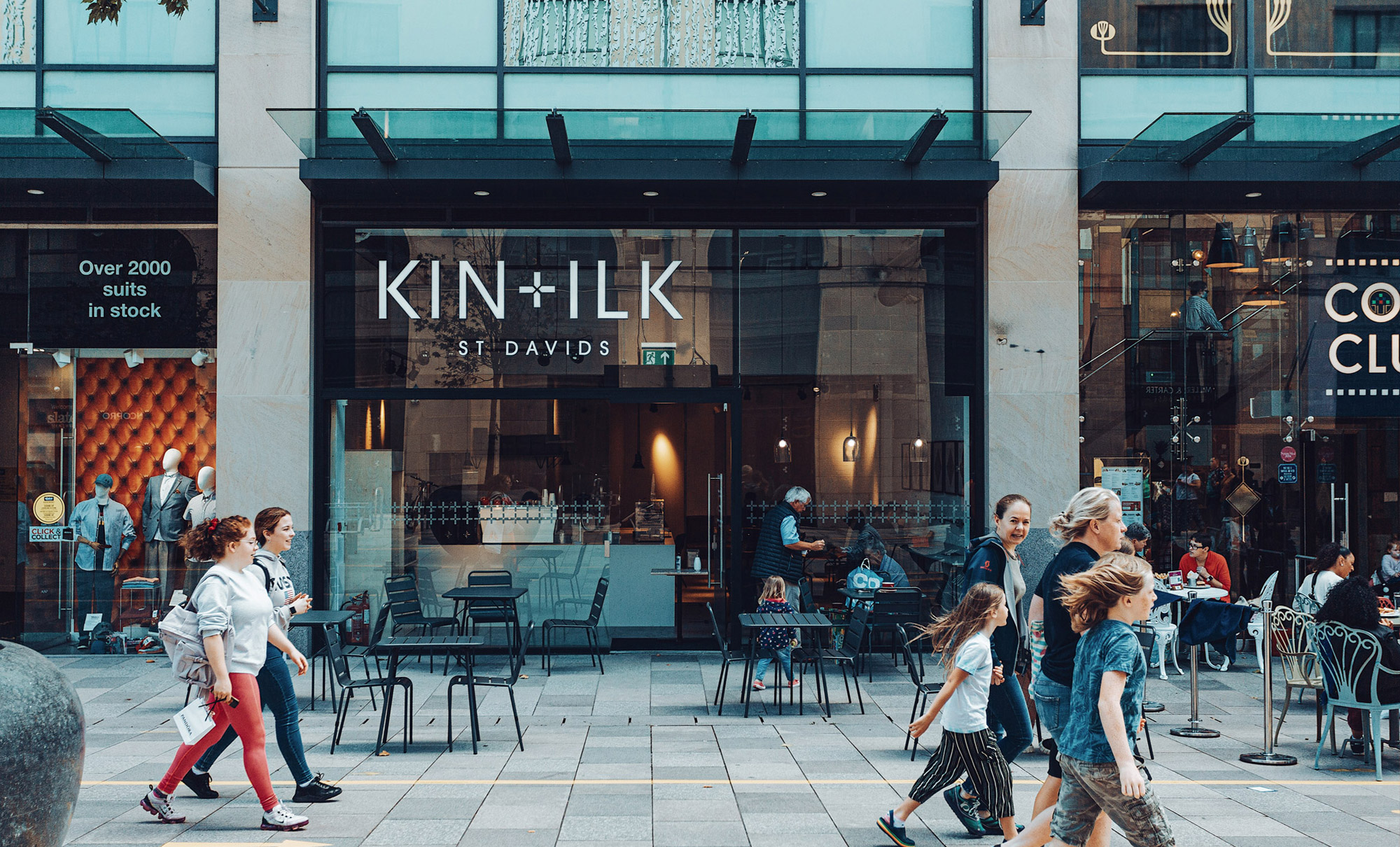 Front of city centre coffee shop with large type and people walking past. 